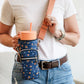 Person holding a floral-patterned crossbody bag with a drink holder.