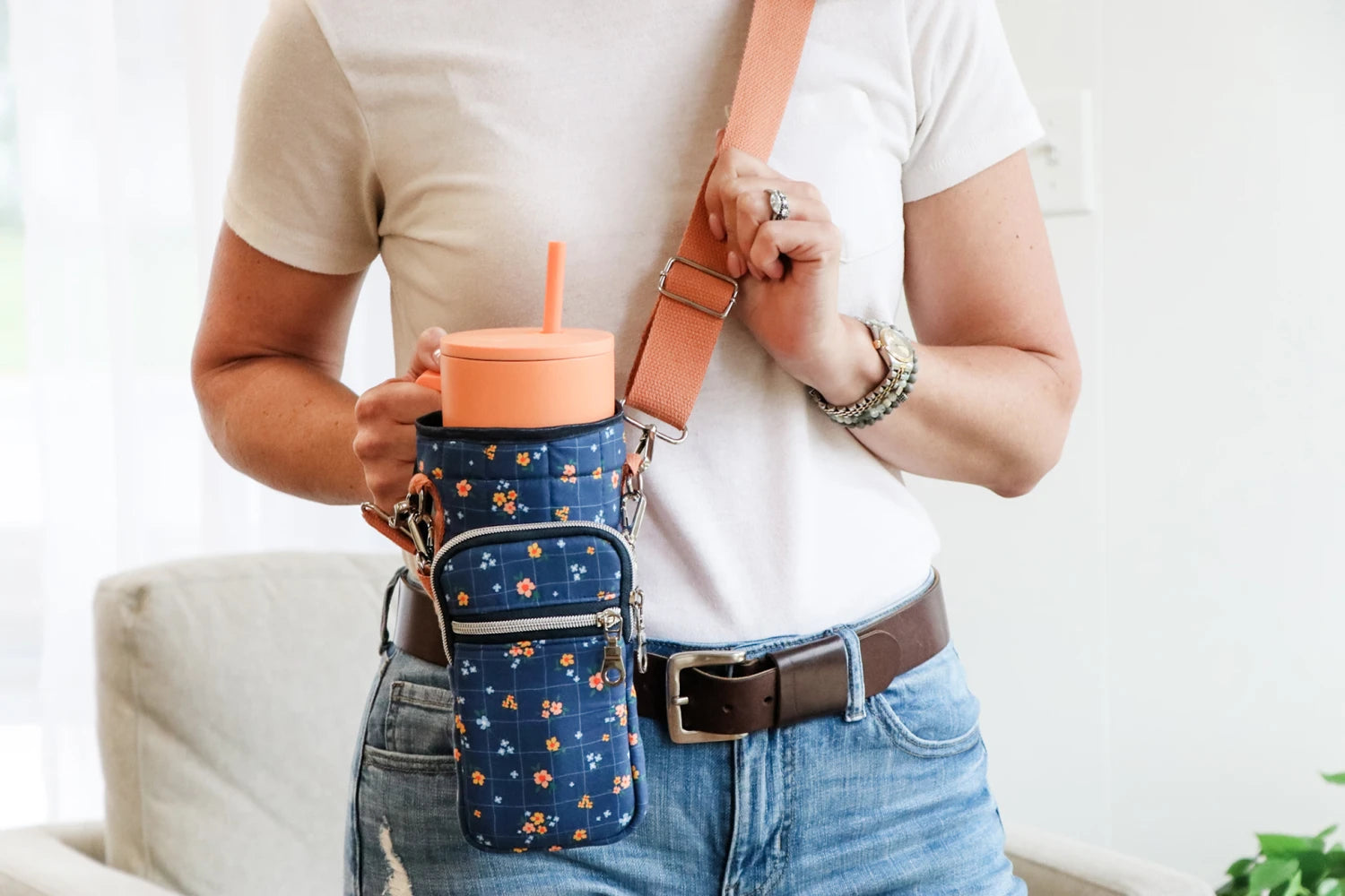 Person holding a floral-patterned crossbody bag with a drink holder.
