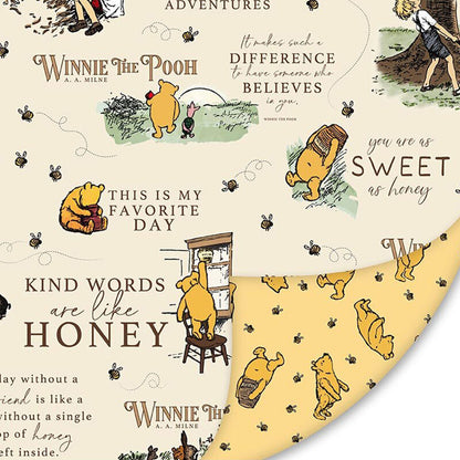 Winnie the Pooh-themed double sided cuddle fabric with illustrations and text on a beige background on one side, and a bear with bees and honey pots on the other.