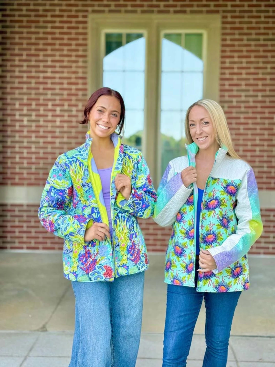 Two women wearing colorful Bell Quilt Coats standing in front of a brick building.