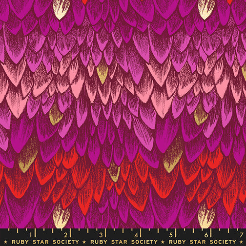 Fabric with pink and red dragon scale pattern, with accents of metallic gold scales and a ruler for scale.