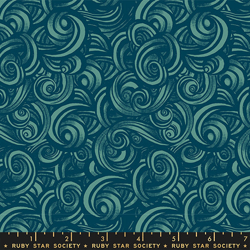 Patterned fabric with swirling designs in teal on a blue background with a ruler for scale.
