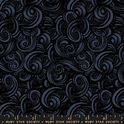 Patterned fabric with swirling designs in gray and black on a black background with a ruler for scale.